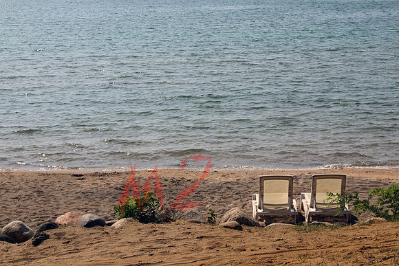 Two Chairs Resting By Rocky Lakeshore and Open Water